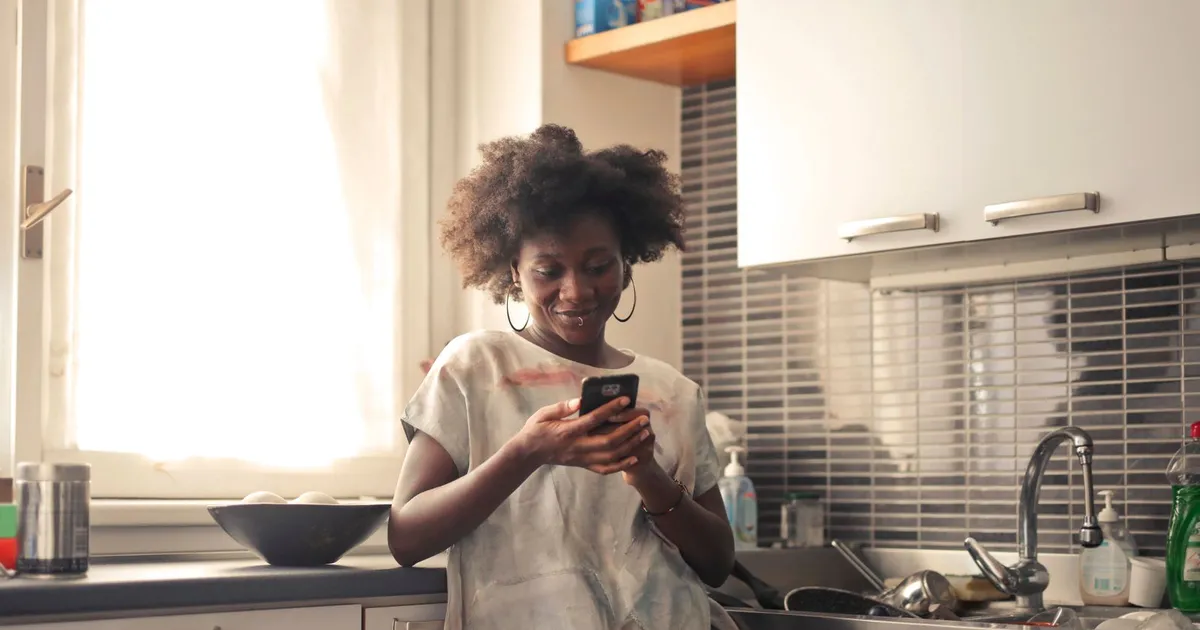 Femme dans sa cuisine qui lit sur son téléphone la décision de son prêt sans enquête de crédit