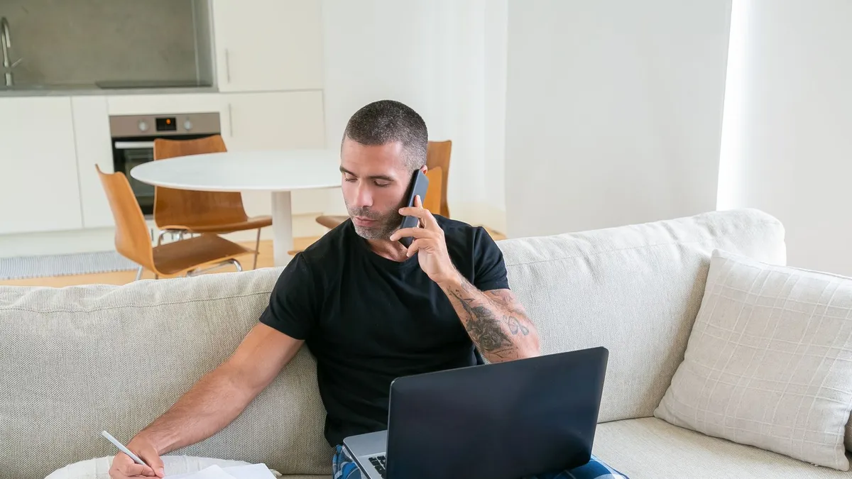 Homme assis sur son divan qui remplit une demande de prêt sans enquête sur son portable et prend des notes